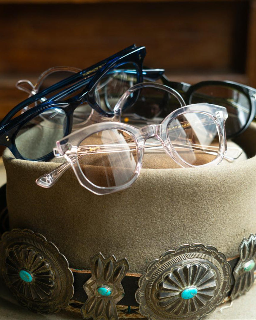 Cowboy hat with decorative conchos holding eyeglasses against a wooden background